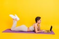 Profile side view portrait of attractive slender cheerful girl lying on mat using laptop  over bright yellow Royalty Free Stock Photo