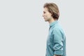 Profile side view portrait of handsome long haired blonde young man in blue casual shirt standing and looking with serious face Royalty Free Stock Photo