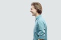 Profile side view portrait of happy handsome long haired blonde young man in blue casual shirt standing and looking with toothy Royalty Free Stock Photo