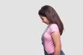 Profile side view portrait of sad alone brunette young girl in casual style, pink t-shirt and blue denim overalls standing, Royalty Free Stock Photo