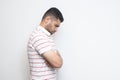 Profile side view portrait of sad alone o depressed bearded young man in striped t-shirt standing, holding his head down and Royalty Free Stock Photo