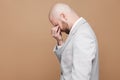 Profile side view portrait of sad crying middle aged bald bearded businessman in light gray suit standing and closed eyes with ha Royalty Free Stock Photo