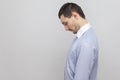 Profile side view portrait of sad depressed handsome bristle businessman in classic blue shirt standing holding head down and