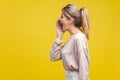 Profile side view of positive beautiful blonde woman with ponytale hairstyle and in casual beige blouse, isolated on yellow Royalty Free Stock Photo