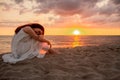 Profile of a single alone or divordes woman silhouette in long white dress sittingon the beach at sunset with her head