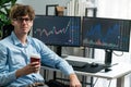 Profile of stock trader sitting against on screen, holding coffee cup. Gusher.