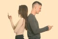 Profile view of angry young couple using mobile phone with backs against each other Royalty Free Stock Photo