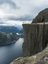 Profile view of famous Preikestolen massive cliff at fjord Lysefjord, famous Norway viewpoint with group of tourists and hikers.