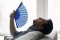 Profile view tired man waving paper fan, suffering from heat