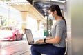 Profile view of young Asian woman with mask using laptop at the bus stop Royalty Free Stock Photo