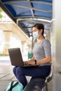 Profile view of young Asian woman with mask using laptop while sitting at the bus stop Royalty Free Stock Photo