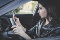 Profile view of young attractive woman looking at her smartphone while driving a car on a warm day. Female driver in