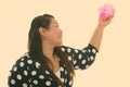 Profile view of young happy fat Asian woman smiling while raising piggy bank Royalty Free Stock Photo