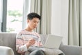 Profile view of young mixed ethnicity man sitting on sofa at home with laptop computer using credit card to shop online Royalty Free Stock Photo