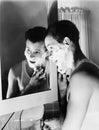 Profile of a young man in front of a mirror in a bathroom shaving