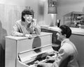 Profile of a young man playing a piano with a young woman standing in front of him and smiling and singing Royalty Free Stock Photo