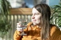 Young pretty caucasian woman holding glass of drinking water in sunlight against backdrop of home plants Royalty Free Stock Photo