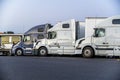 Profiles of big rigs semi trucks with semi trailers standing in row on evening truck stop parking lot Royalty Free Stock Photo