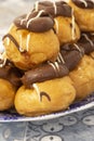 Profiteroles, coated in chocolate, stacked on a pattermed blue and white plate. Royalty Free Stock Photo