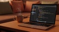 Programmer working on laptop with coffee on wooden table in cozy living room Royalty Free Stock Photo