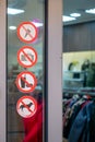 Prohibition signs near the entrance to the clothing store. Stickers on the glass window near the door with prohibitions.