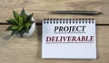 PROJECT DELIVERABLE - words are written in a notebook with a pen, on a wooden background with a cactus Royalty Free Stock Photo