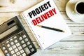 PROJECT DELIVERY written on white paper near coffee and calculator on a light wooden table. Business concept Royalty Free Stock Photo