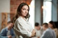 Project manager. Serious ambitious young woman in formal wear attentively looking at camera. Blurred employees on