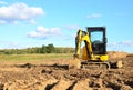 Mini excavator digging earth in a field or forest.