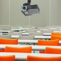 A projector over empty seats with tables in a conference hall.