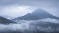 Prominent mountain covered by forest and shrouded by a thick fog on a moody autumn morning