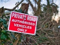 A prominent sign of white words on a red background in a hedgerow advises that the road ahead is private