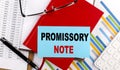 PROMISSORY NOTE text on a sticky on red notebook on chart background