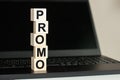 PROMO word made with building blocks on the black keyboard. A row of wooden cubes with a word written in black font is located on