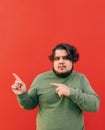 Promotional vertical photo of a young serious hispanic obese man pointing his fingers at a red background, feeling confident Royalty Free Stock Photo