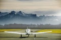 Propeller plane parking at the airport. Small airfield in front of high mountains. Sunset over mountains. Royalty Free Stock Photo