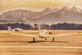 Propeller plane parking at the airport. Small airfield in front of high mountains. Sunset over mountains. Royalty Free Stock Photo