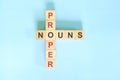 Proper Nouns concept in English grammar education. Wooden block crossword puzzle flat lay in blue background.