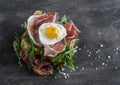 Prosciutto, arugula, and fried quail eggs sandwich on wooden background, top view.