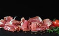 Prosciutto crudo or jamon meat with rosemary on serving board on black background. Sliced into thin pieces of ham Royalty Free Stock Photo