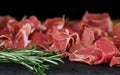 Prosciutto crudo or jamon meat with rosemary on serving board on black background. Sliced into thin pieces of ham puts on cutting Royalty Free Stock Photo