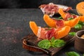 Prosciutto ham with melon cantaloupe slices, honey and basil on cutting board over dark background. Italian appetizer Royalty Free Stock Photo