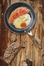 Prosciutto Rashers With Fried Egg In Frying Pan With Slice Of Brown Bread Set On Old Cracked Wooden Garden Table