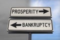 Prosperity versus bankruptcy road sign with two arrows on blue and grey sky background. White two street sign with arrows on metal Royalty Free Stock Photo