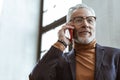 Prosperous businessman calling his partner standing near window