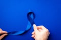 Prostate care. Awareness prostate cancer of men health in November. Blue ribbon in hands isolated on deep blue background. World