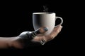 Prosthetic or robotic hand holding a cup of coffee or tea on a black background. A bionic robot hand holding a cup