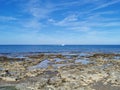 Long-hardened lava, the shore of the Mediterranean Sea against the backdrop of the sea with a white yacht and a blue sky with Royalty Free Stock Photo