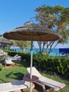 A parasol made from natural materials reeds or reeds, sun loungers with mattresses on the grass, wood and a blue cloudless sky