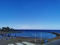 A small municipal beach in the bay of the Mediterranean Sea with sun loungers and closed parasols against the blue sky